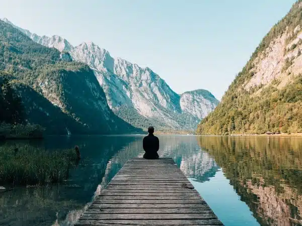 man sitting on a dock overlooking a lake and mountains