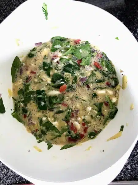 eggs, spinach, red peppers, and feta cheese mixed in a bowl