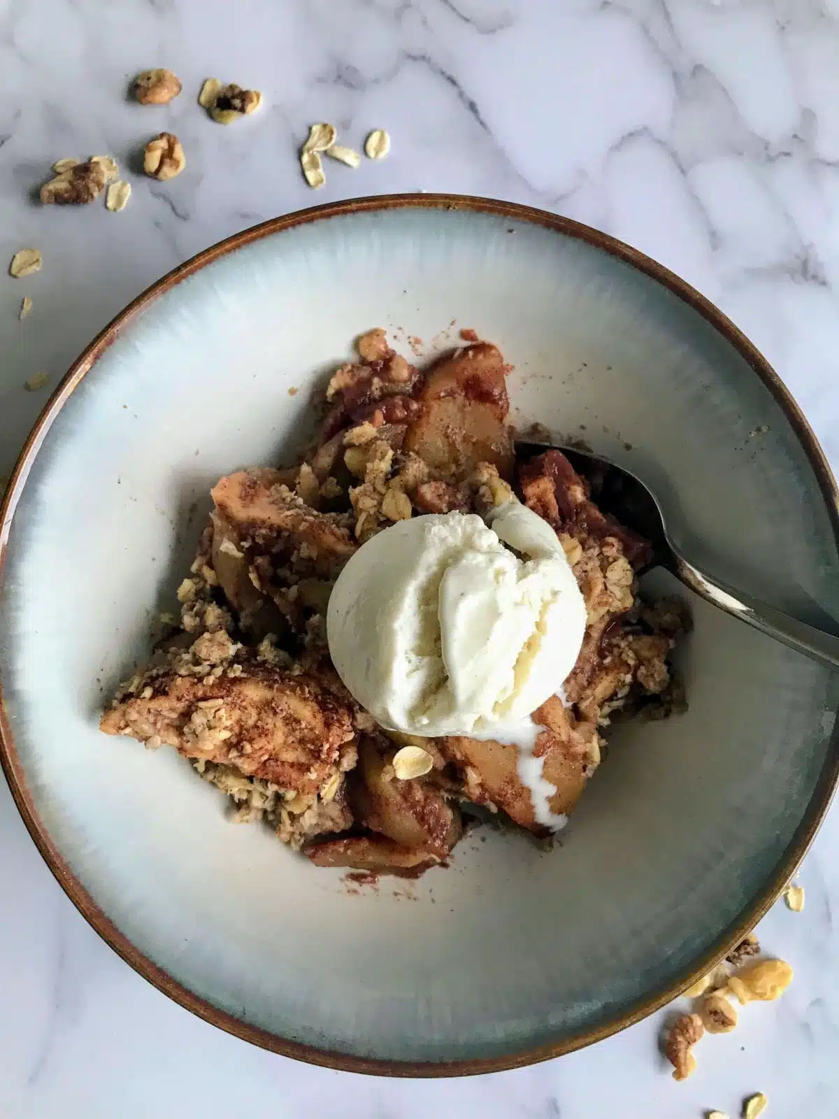 warm maple walnut apple crisp in a bowl with a scoop of vanilla ice cream on top