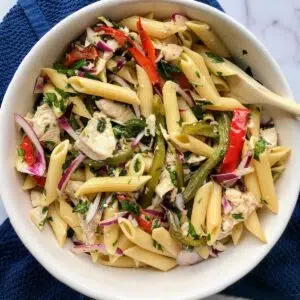 chicken bell pepper pasta salad in a white bowl with a wooden spoon.