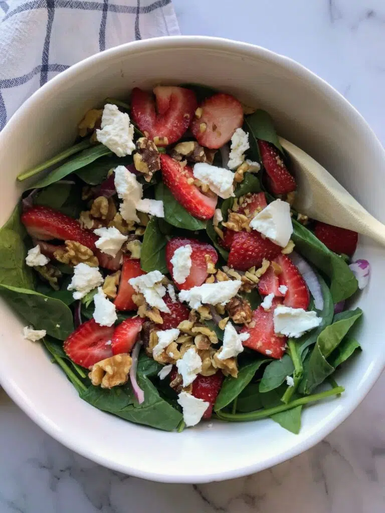 strawberry goat cheese salad with walnuts and spinach in a white bowl.