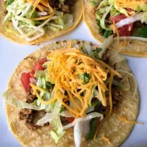Tacos with corn tortillas, shredded lettuce, cheese, and tomatoes.