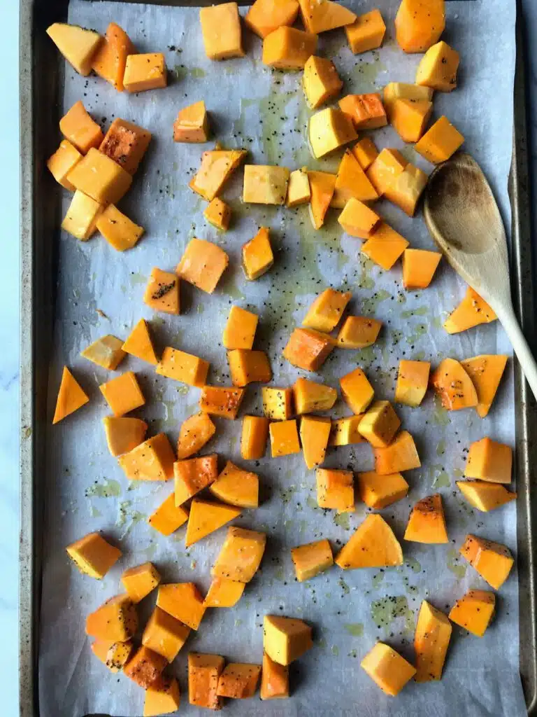 Butternut squash cubes tossed with oil, salt, and pepper on a baking sheet.