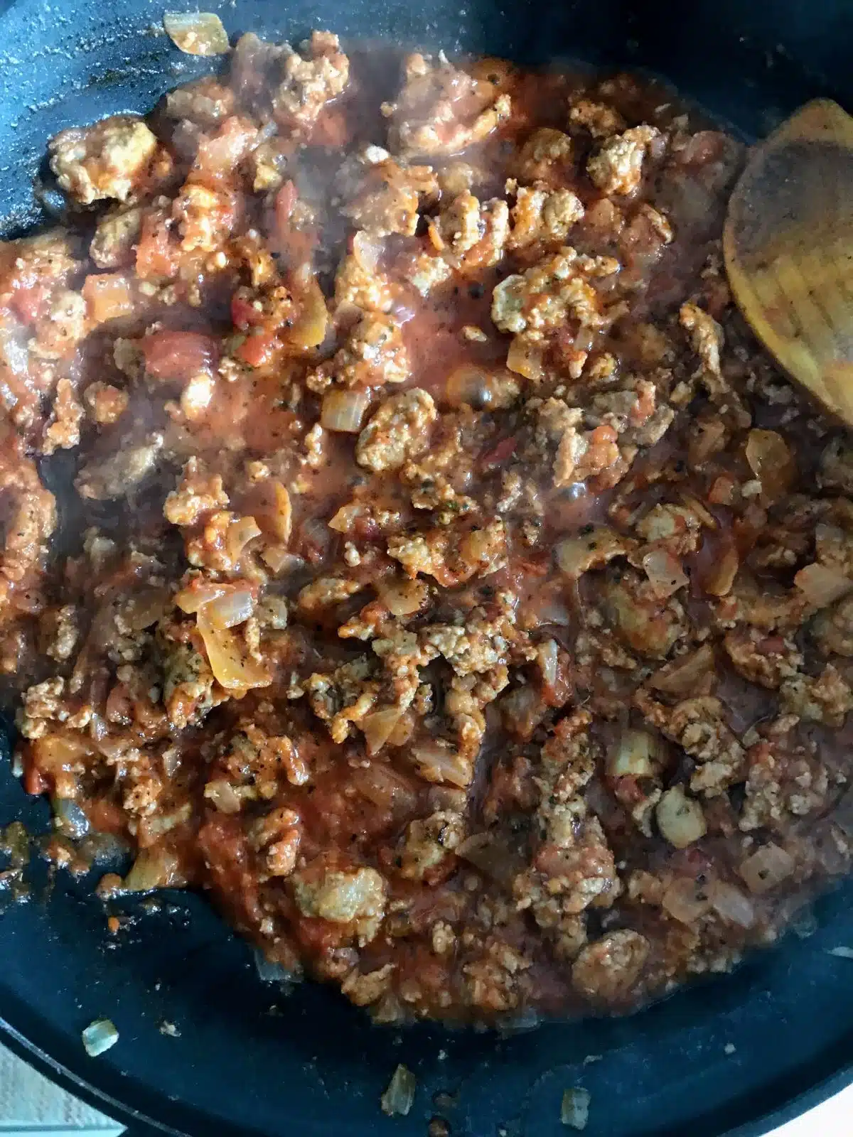 Italian sausage cooking with onions and tomato sauce.